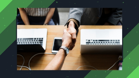 two people shaking hands next to open computers